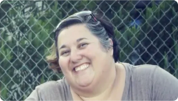 bir zincir bağlantı çitinin önünde gülümseyen bir kişi